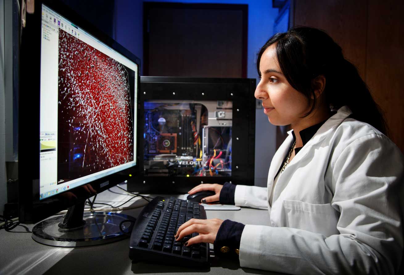 a woman in a white lab coat sits at a computer